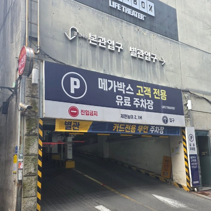 칸세이스시 상무본점 외관 — 메가박스 주차장 입구. '메가박스 고객 전용 유료 주차장' 현수막과 '본관입구·별관입구' 벽 글자, '별관 카드전용 무인 주차장' 안내, 높이 제한 2.1M 표시 아래로 내려가는 진입로가 보인다.